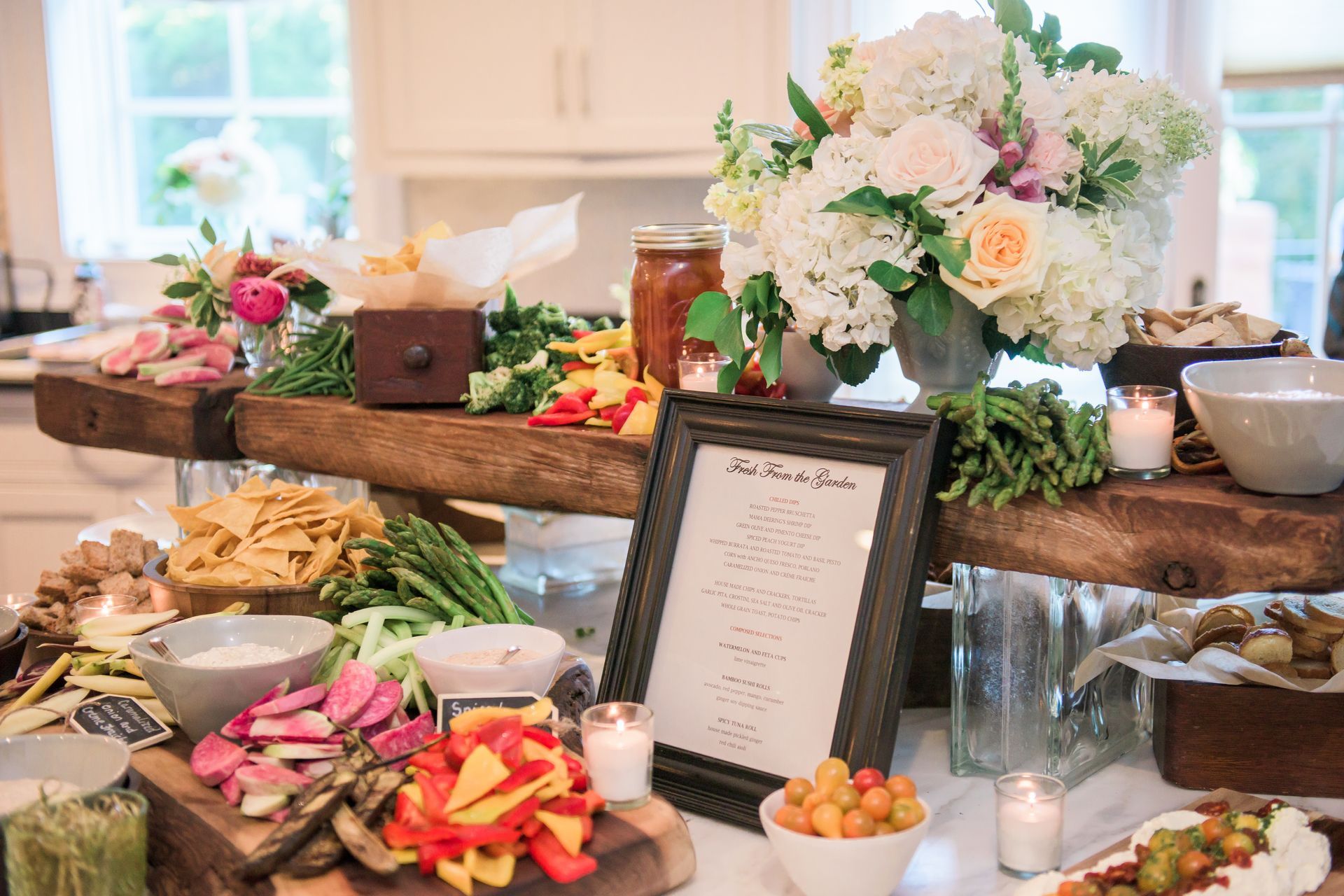 Elegant buffet table with flowers, appetizers, fruit, and a menu sign at a bright indoor event