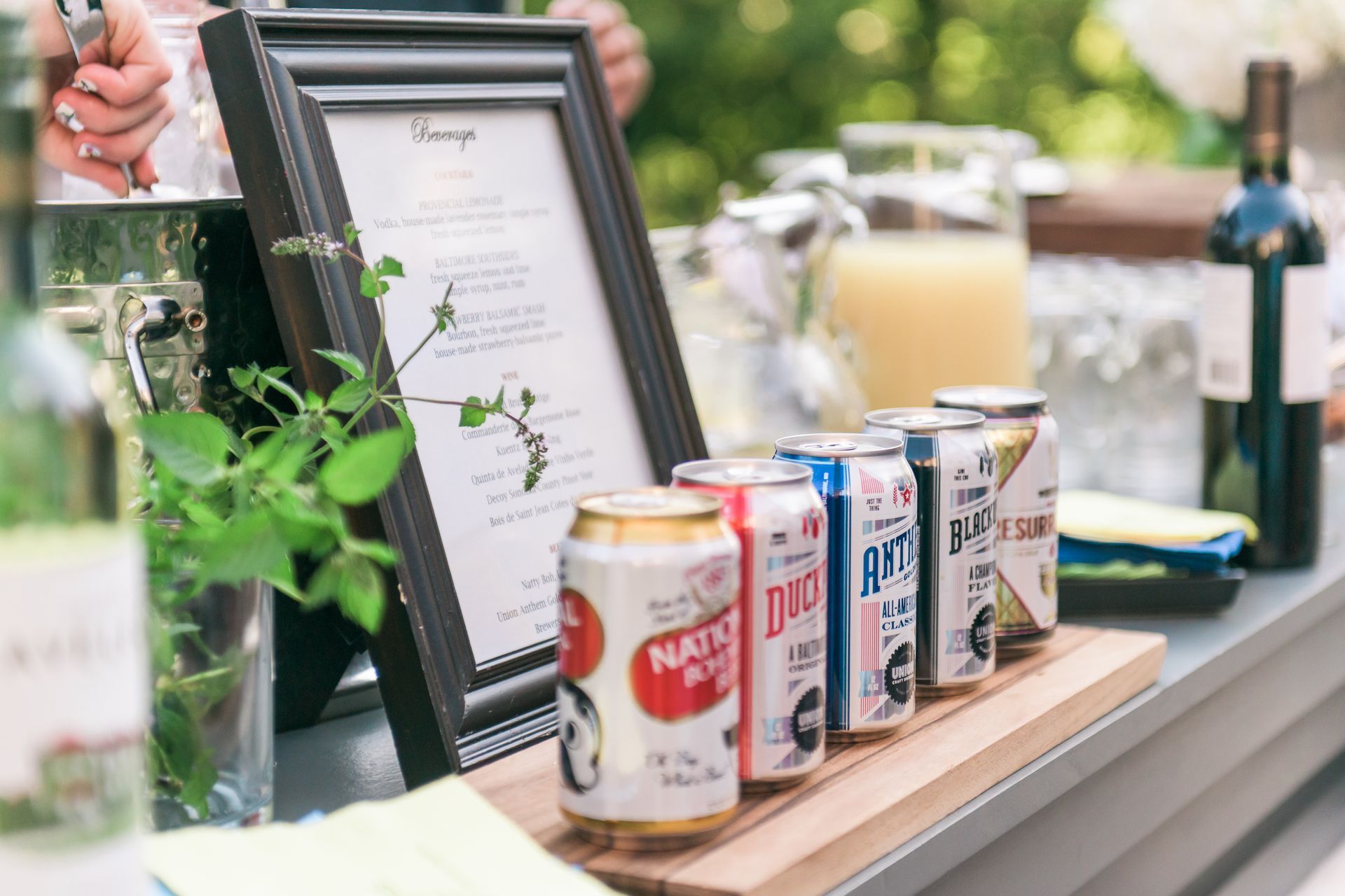 Beer cans and a framed sign displayed on a wooden tray at an outdoor table.