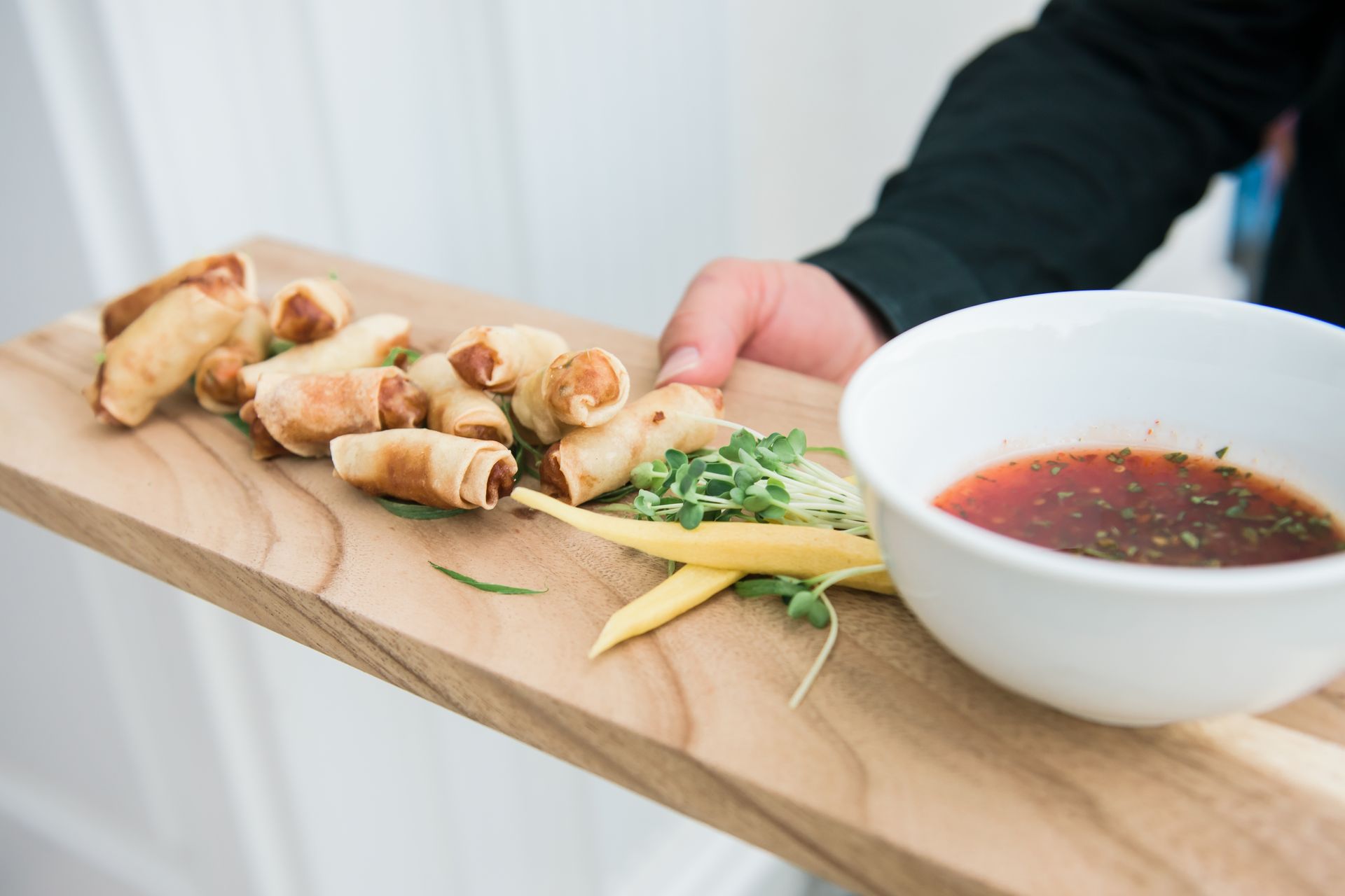 Spring rolls on a wooden tray with dipping sauce and garnish