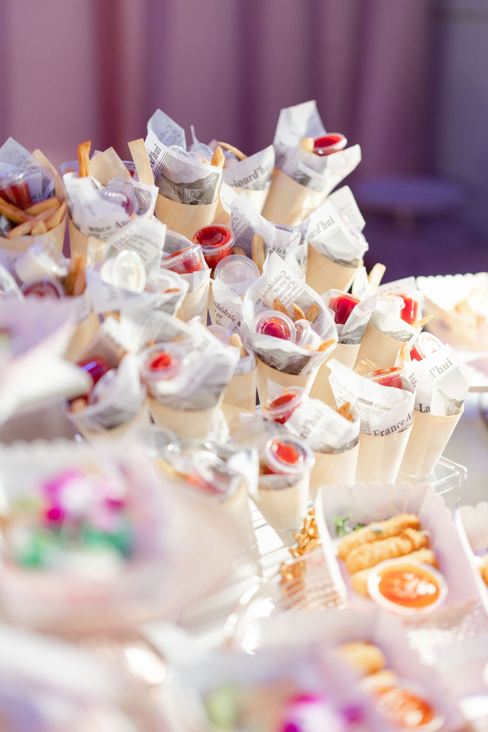 Rows of small white favor bags with red and orange treats at a softly lit event table