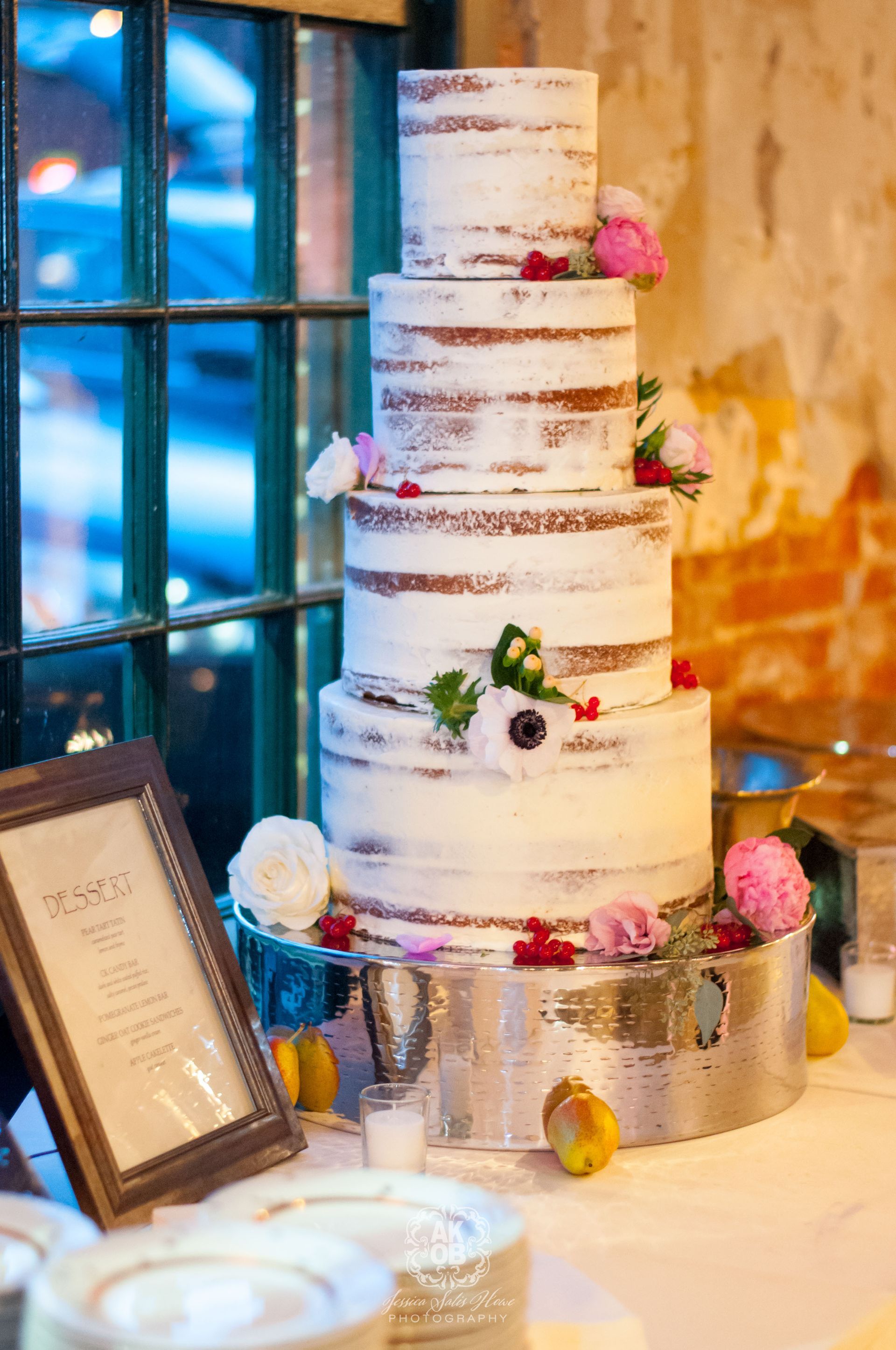 Tall white tiered wedding cake with pink flowers on a decorated dessert table