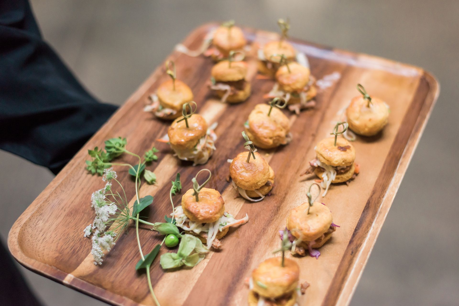 Tray of bite-sized appetizers topped with herbs, arranged on a wooden serving platter