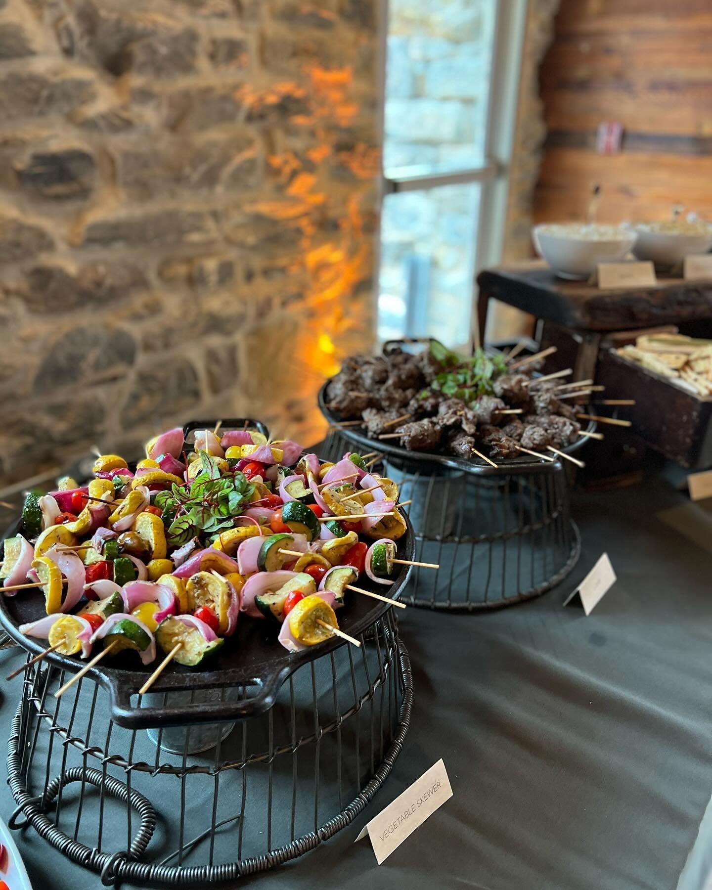 Colorful skewered appetizers on wire stands beside a bowl of rustic decor in a warm stone-walled room