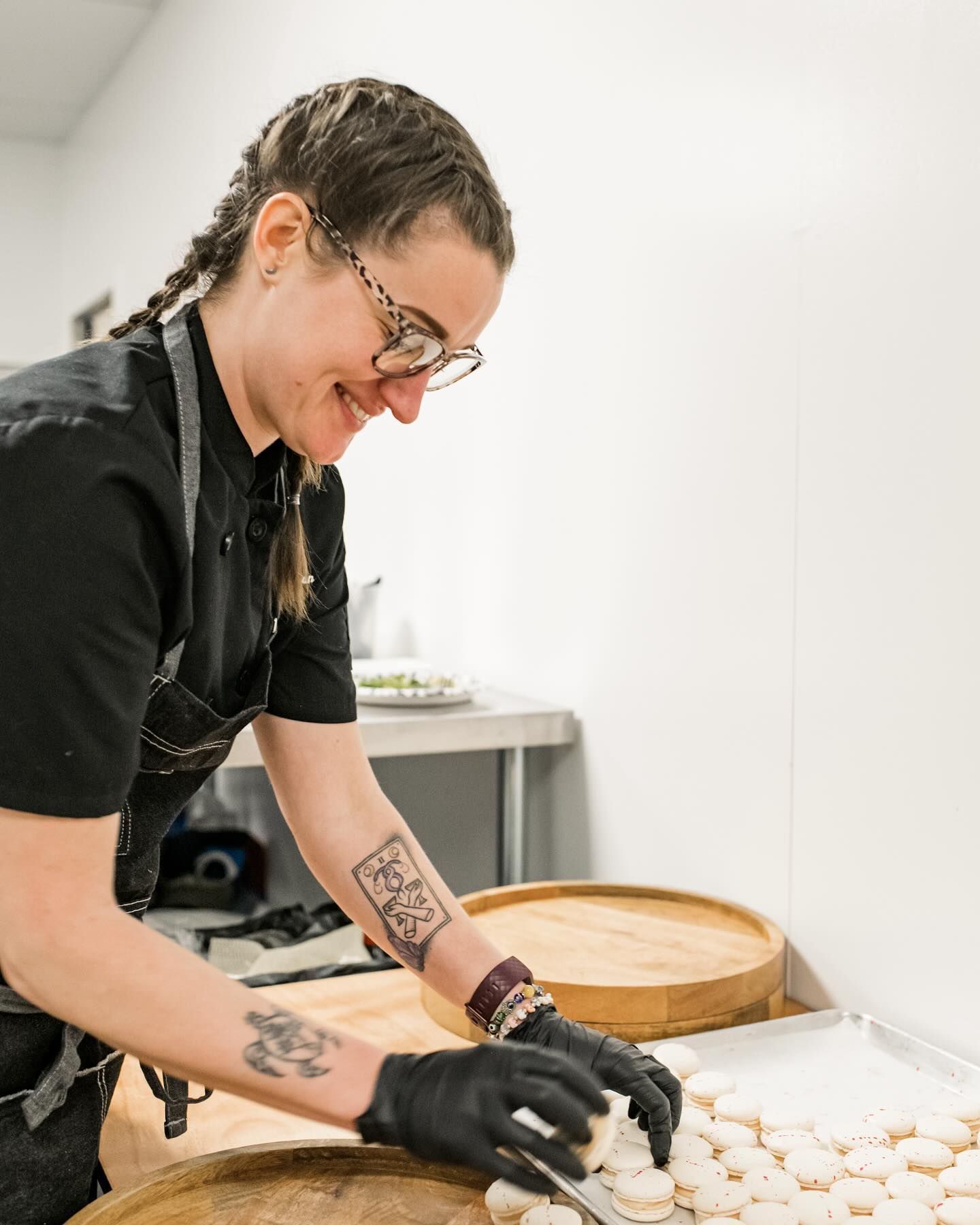 Person in black gloves shaping dough pieces on a worktable in a bright kitchen or bakery.