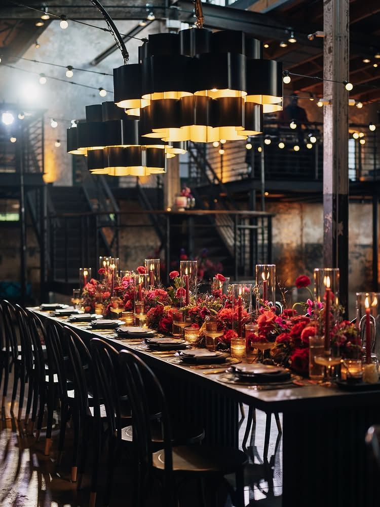 Long dining table with black chairs and red floral centerpieces in an industrial loft venue