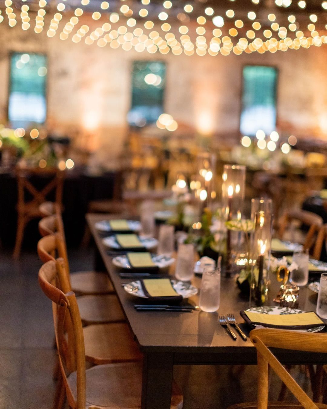 Elegant banquet table set with candles and glassware under warm string lights in a softly lit venue