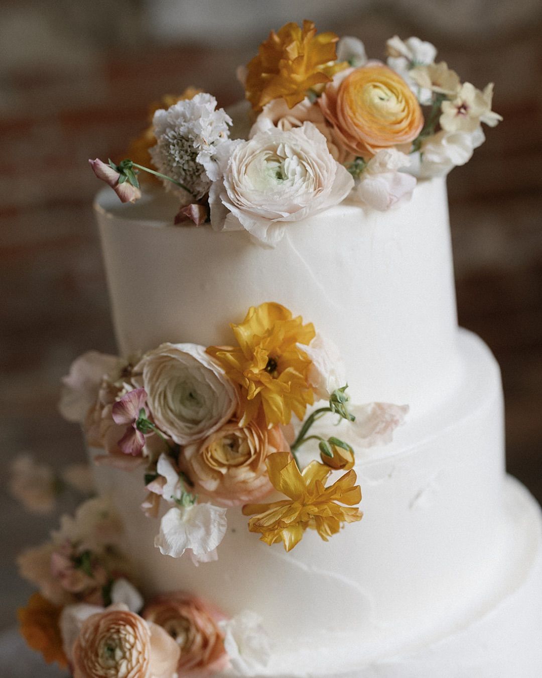 White tiered cake decorated with cream, yellow, and peach flowers