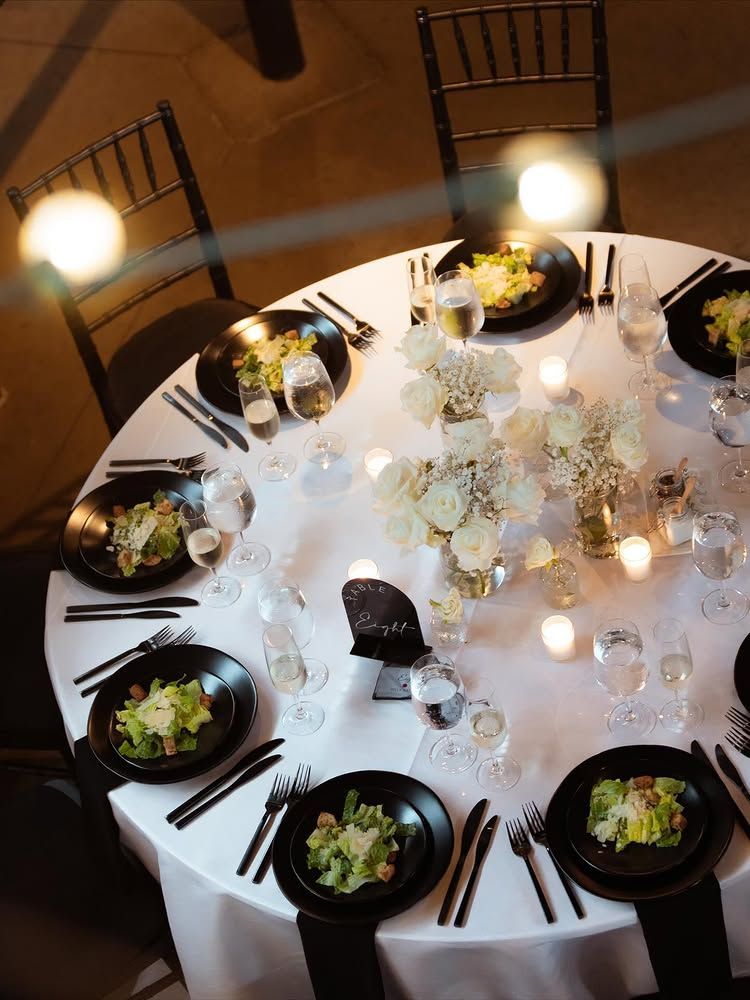 Round dinner table set with plates, glasses, candles, and bowls of salad in a warmly lit dining room