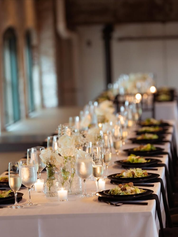 Elegant candlelit banquet table with white tablecloth, glassware, and black napkins in a warm indoor venue
