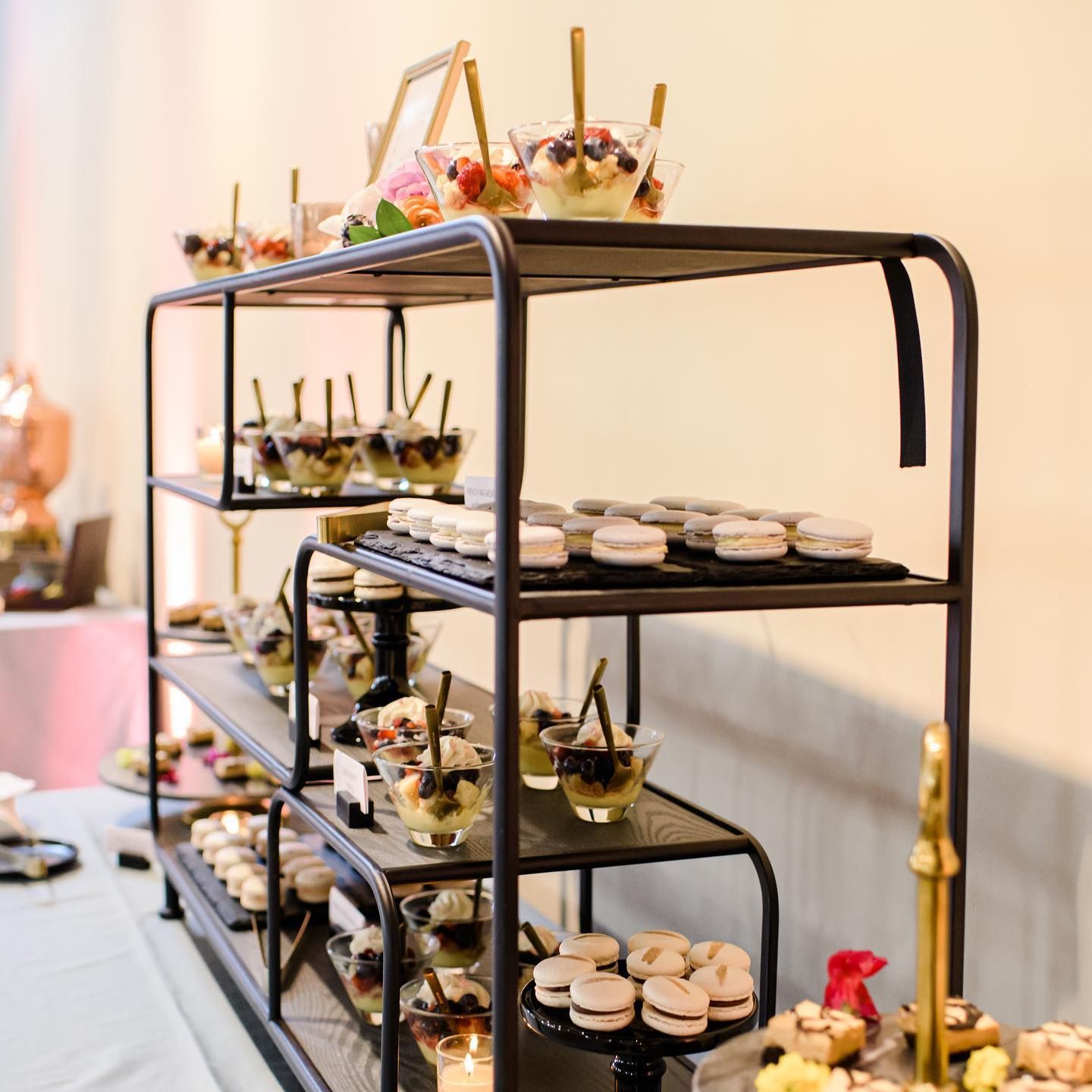 Tiered dessert display with cups and pastries on black metal shelves in a bright room
