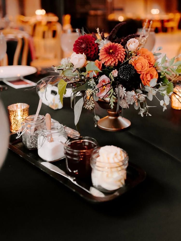 Floral centerpiece on a banquet table with candles, dessert cups, and a black serving tray