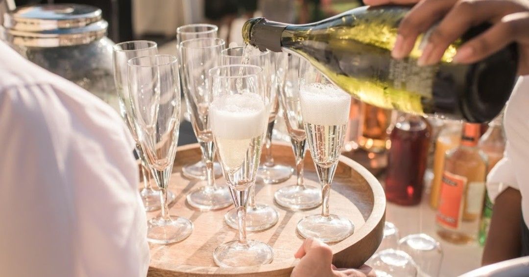 Champagne being poured into glasses at a party table with a champagne bucket and bottles nearby