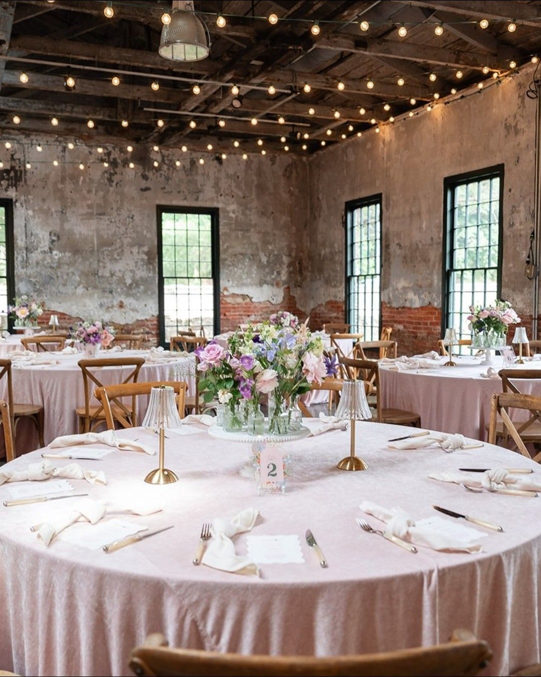 Elegant banquet hall with round tables, white linens, floral centerpieces, and string lights overhead