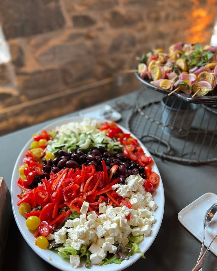 Colorful salad bowls with red peppers, greens, tomatoes, and cheese on a table, with a brick wall backdrop