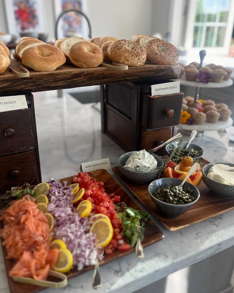 Buffet table with assorted breads, bagels, smoked salmon, cheese, and toppings on platters and bowls