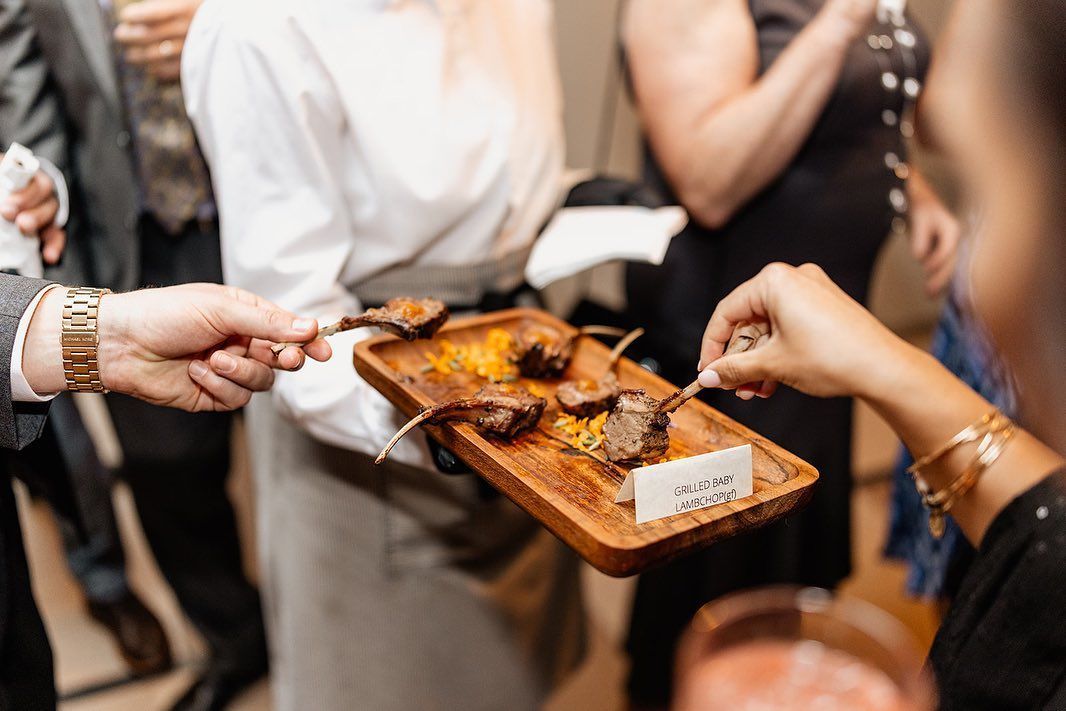 People serving food samples on a wooden tray at a social gathering