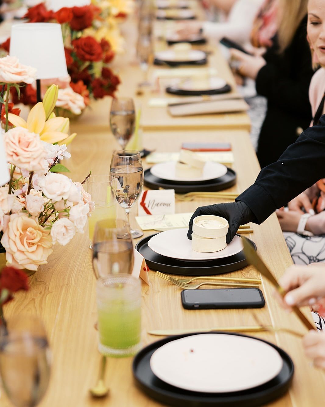 Set dining table with flowers, plates, drinks, and a hand placing butter at a formal event