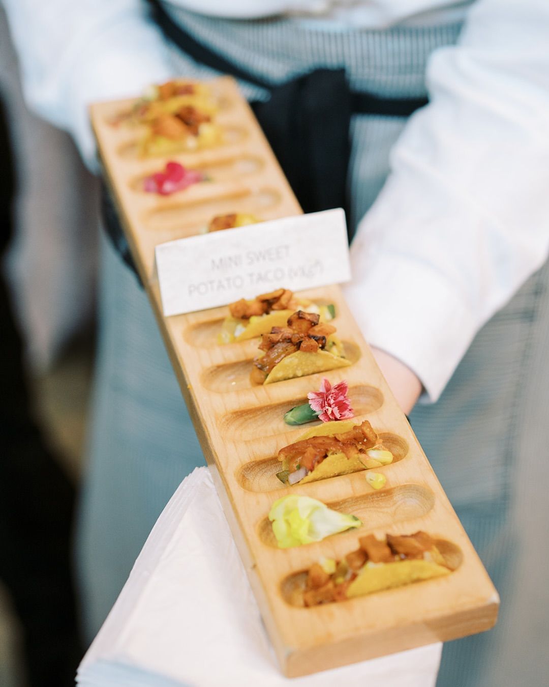 Tray of assorted appetizers on a server’s hands, with a small label card and colorful garnishes.