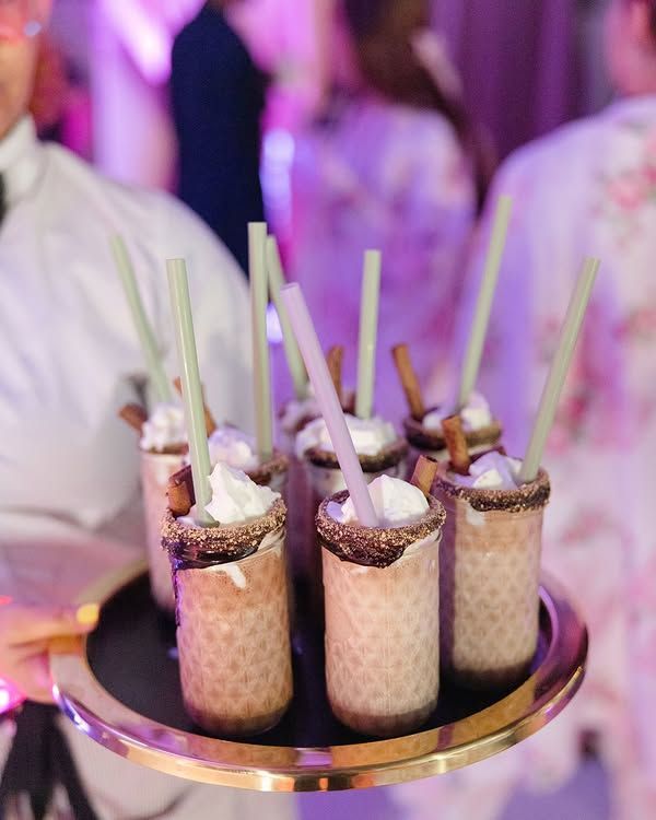 Tray of chocolate-topped milkshake drinks with straws at a party, lit in purple.