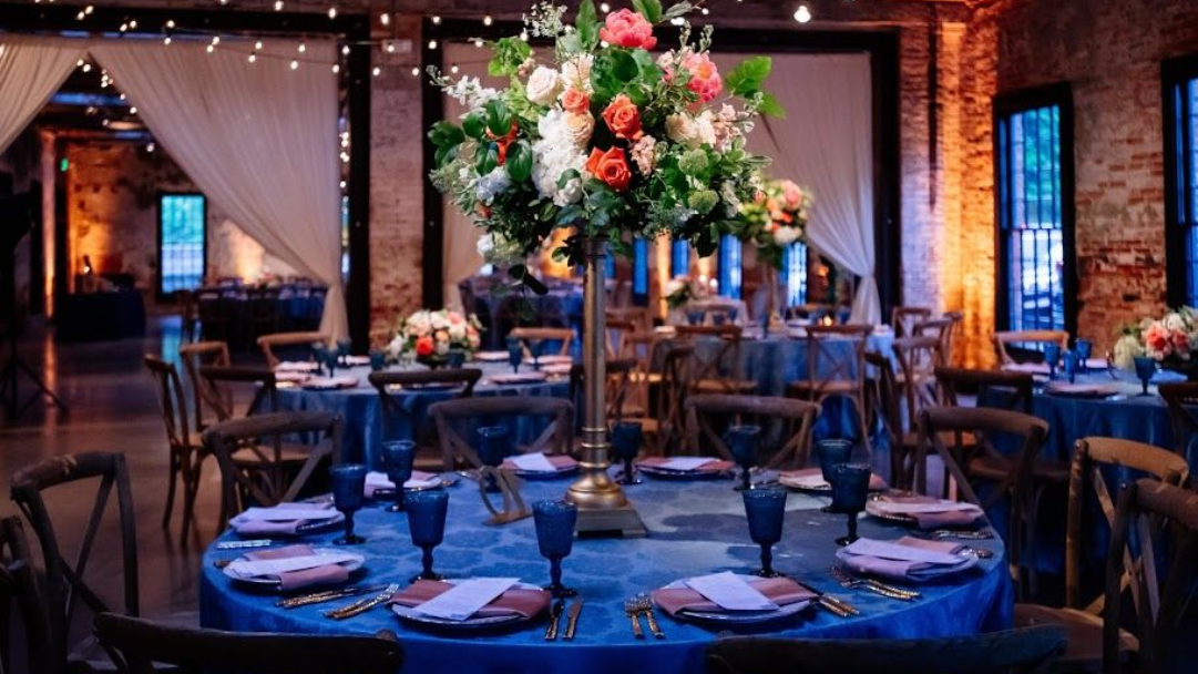Elegant banquet hall with round tables, blue table settings, and a tall floral centerpiece