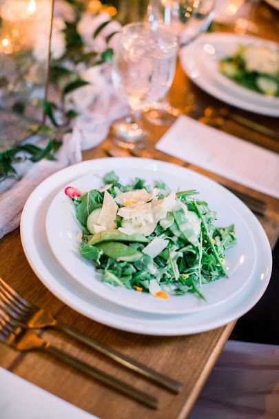 Salad on a white plate at a warmly lit dinner table with glassware and cutlery