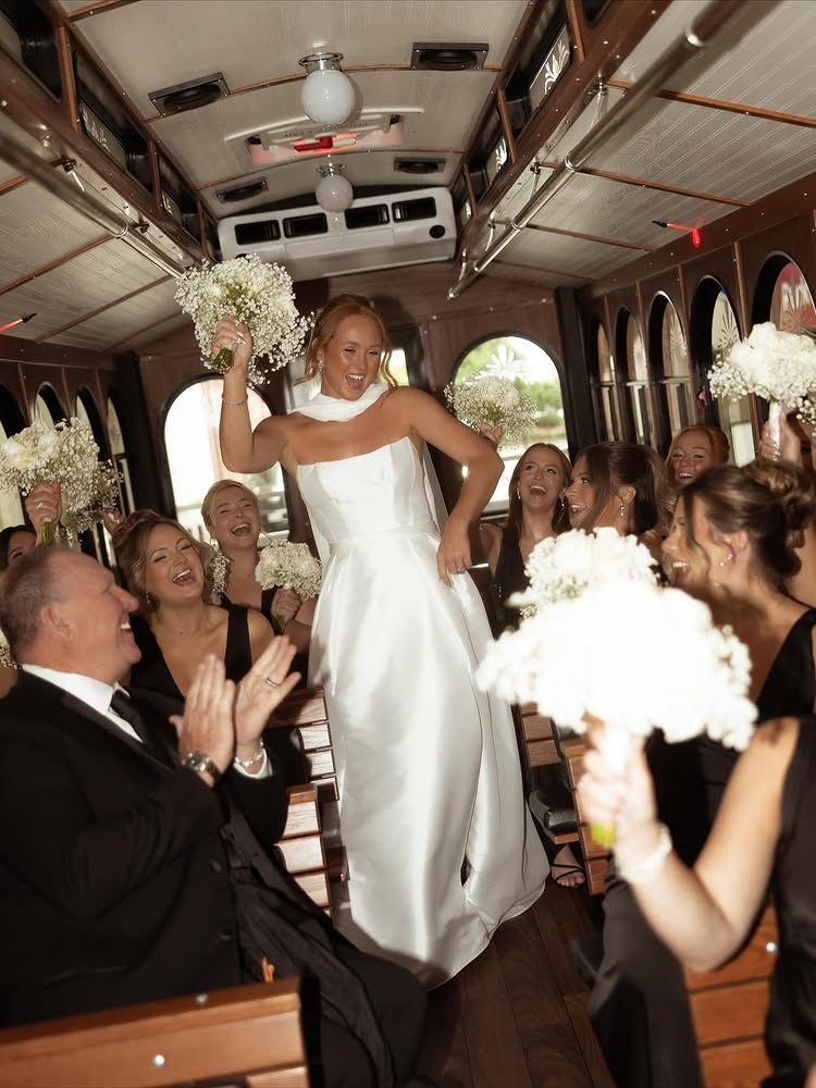 Bride dancing joyfully on a decorated bus surrounded by cheering wedding guests