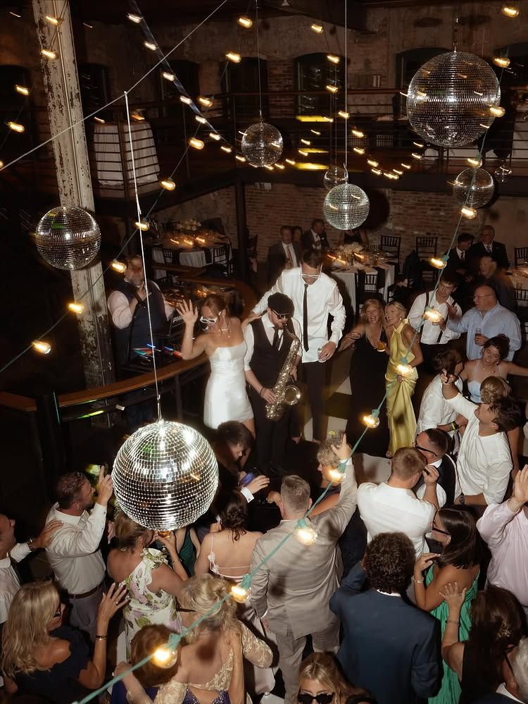 Wedding reception with a bride and groom dancing under hanging disco balls in a crowded, dimly lit venue