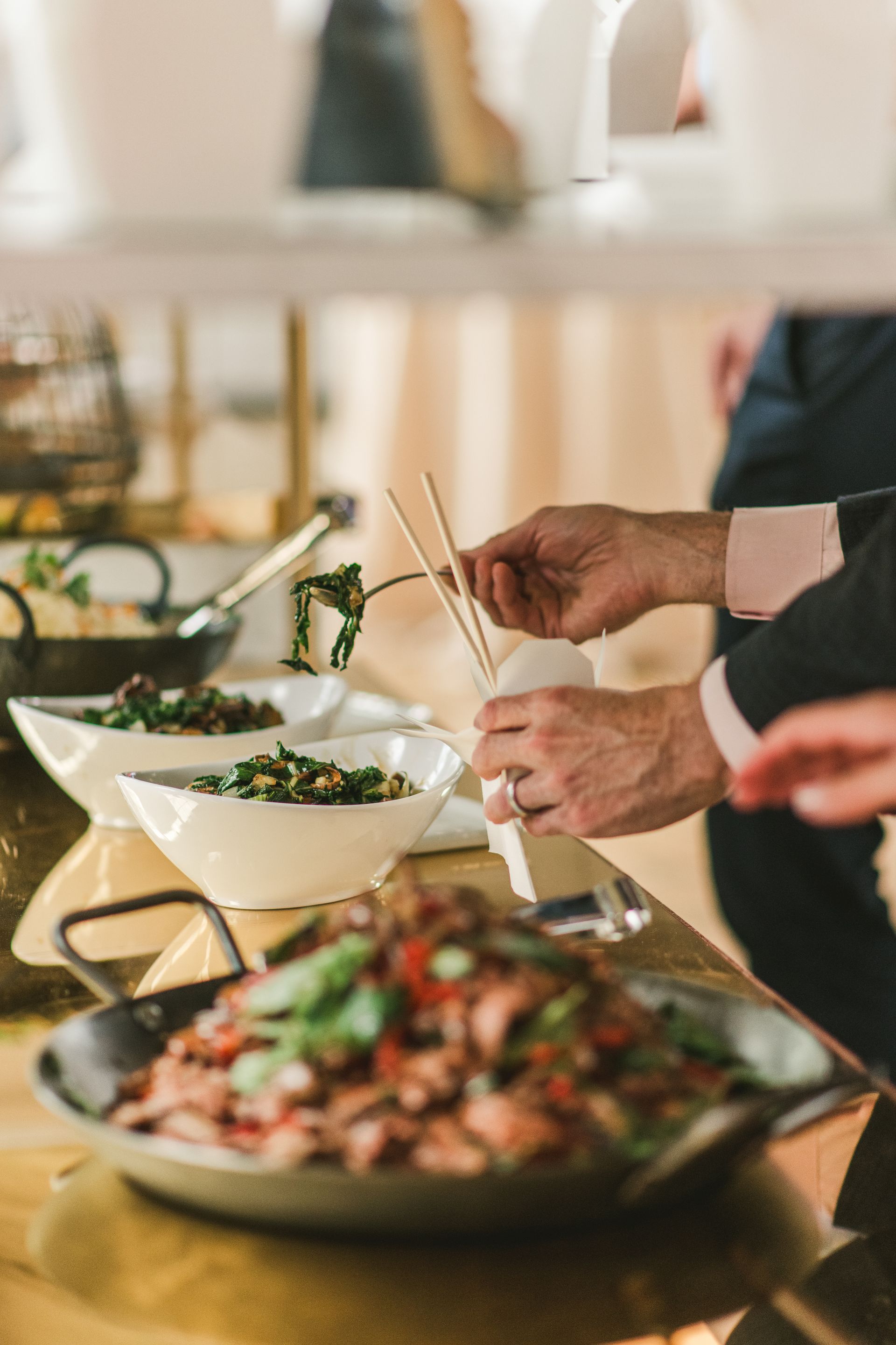People serving dishes at a buffet table with bowls of salad and a platter of food