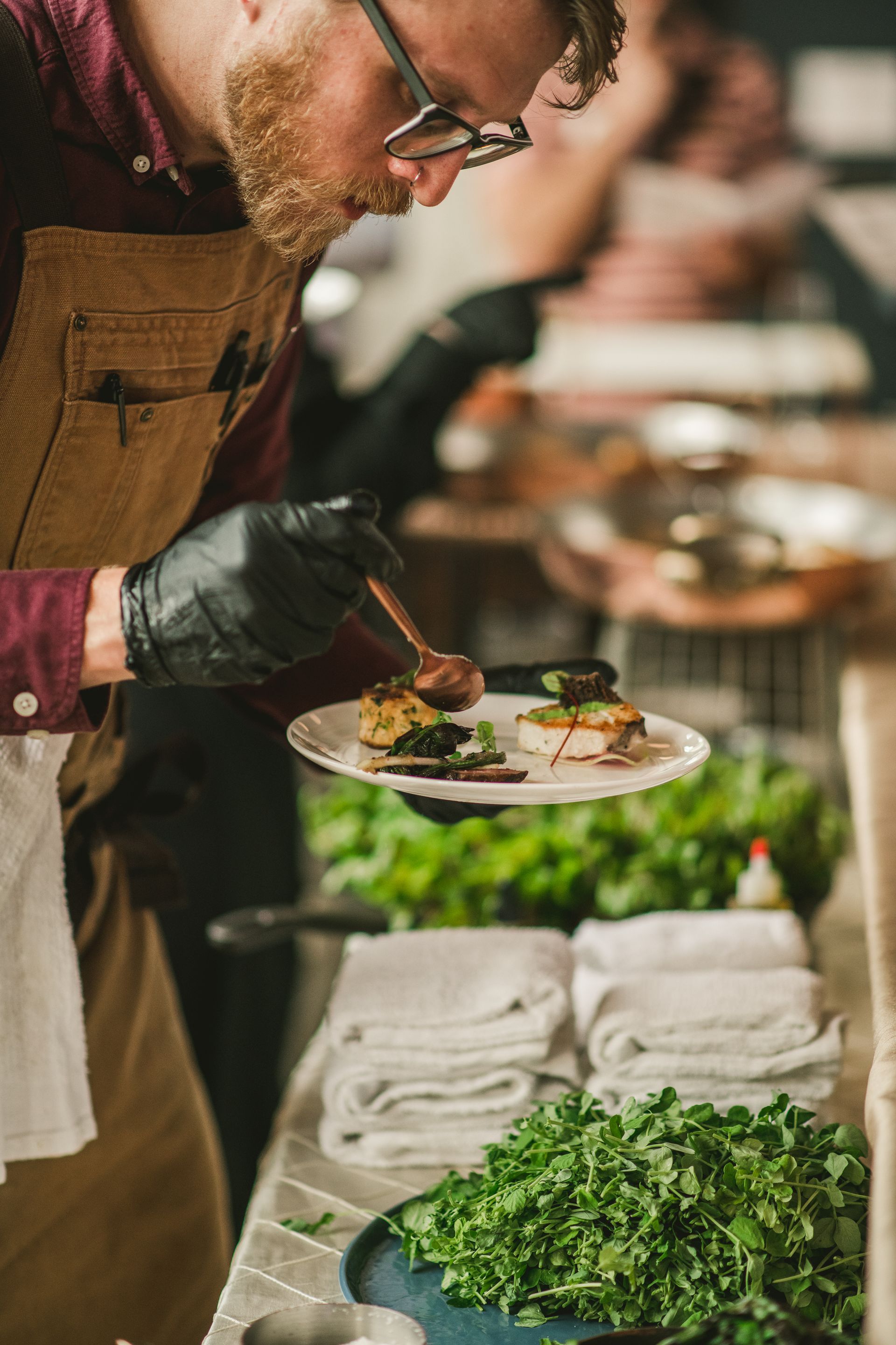 Chef plating a gourmet dish at a buffet, with fresh greens and stacked plates nearby