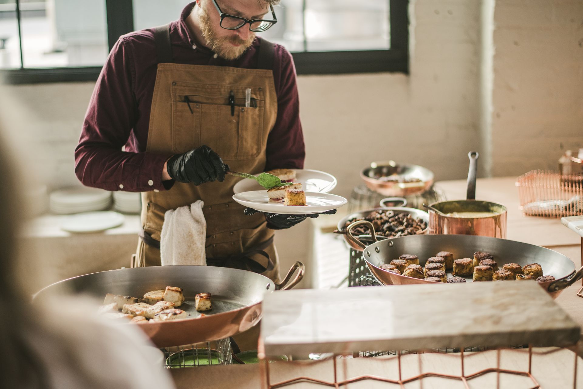 Person serving food at a buffet table with bowls and plates in a bright room