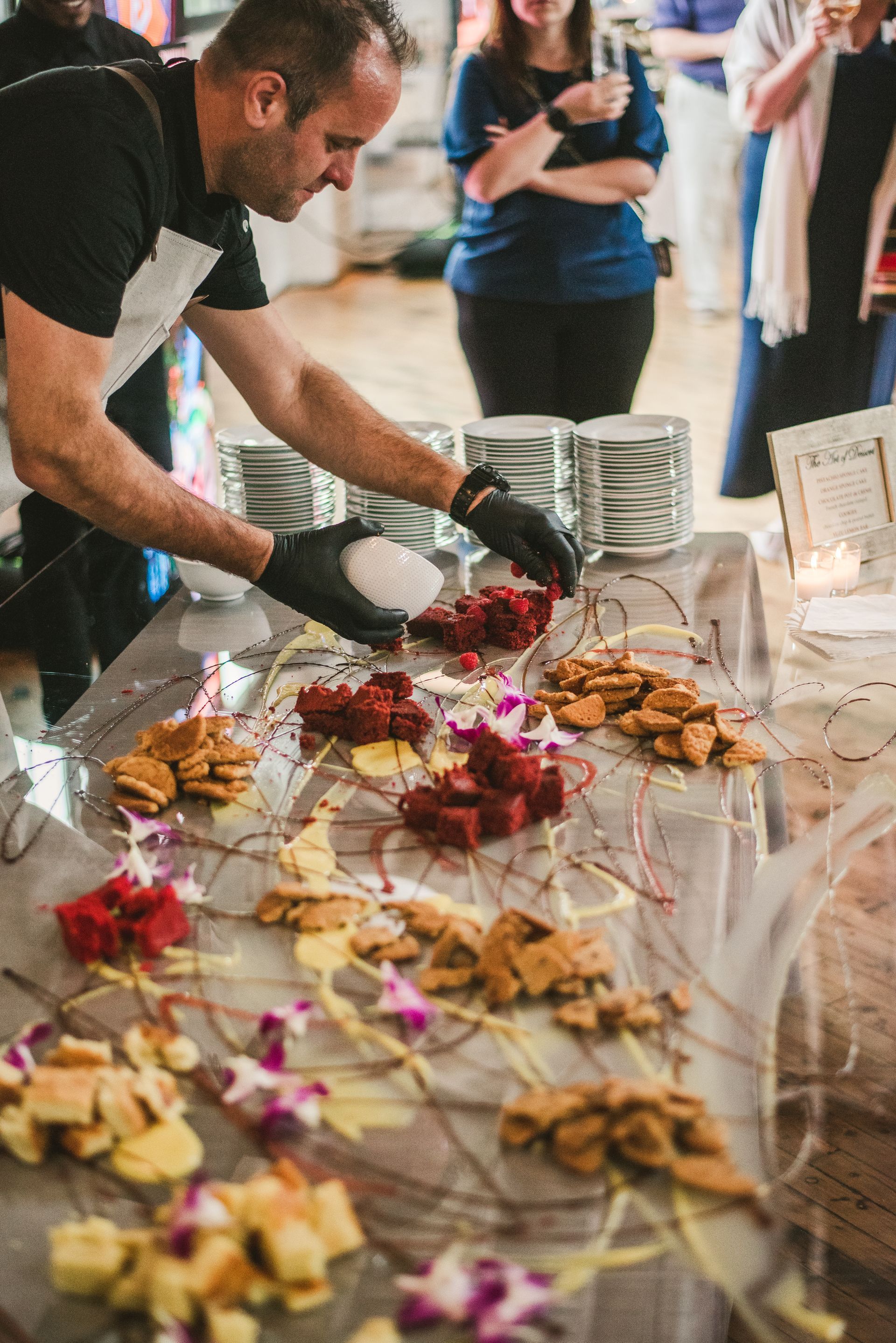 Man serving desserts from a table at a crowded event, with pastries and trays displayed on white cloth
