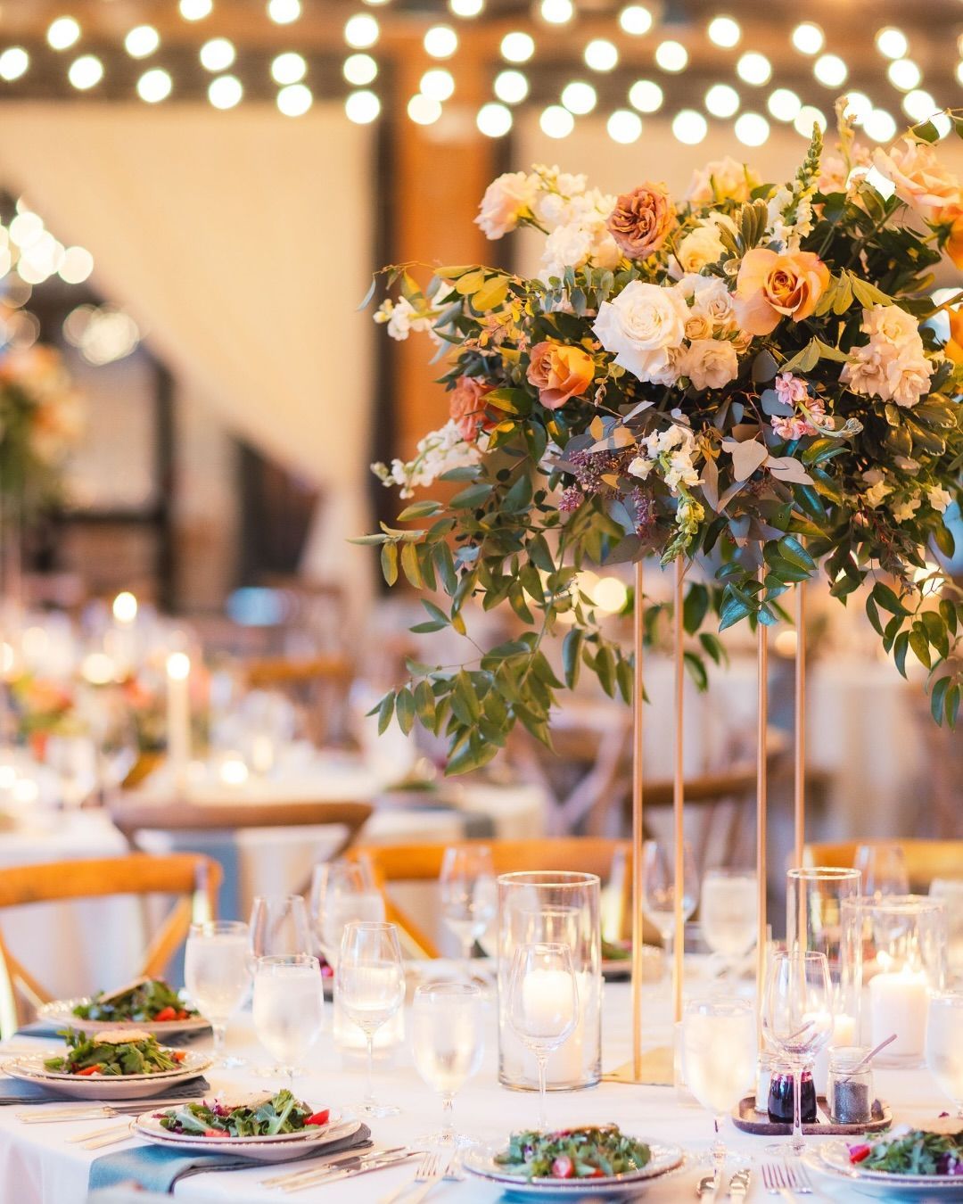 Elegant banquet table with tall floral centerpiece, candles, and warm string lights at a reception