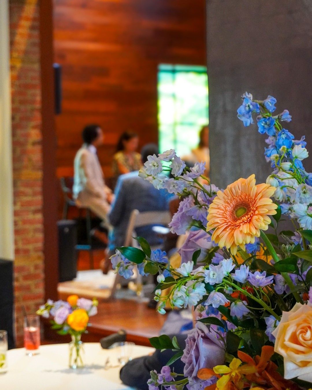 Flowers on a table in a cafe, with people seated in the blurred background.