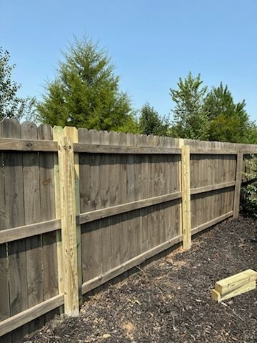 Wooden fence with new, light-colored posts; trees in the background under a blue sky.