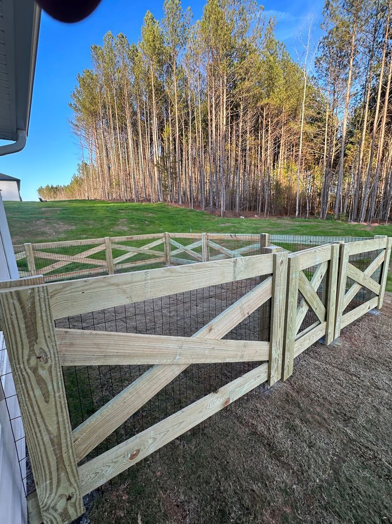 Wooden X-style fence in a yard, trees in background, sunny day.