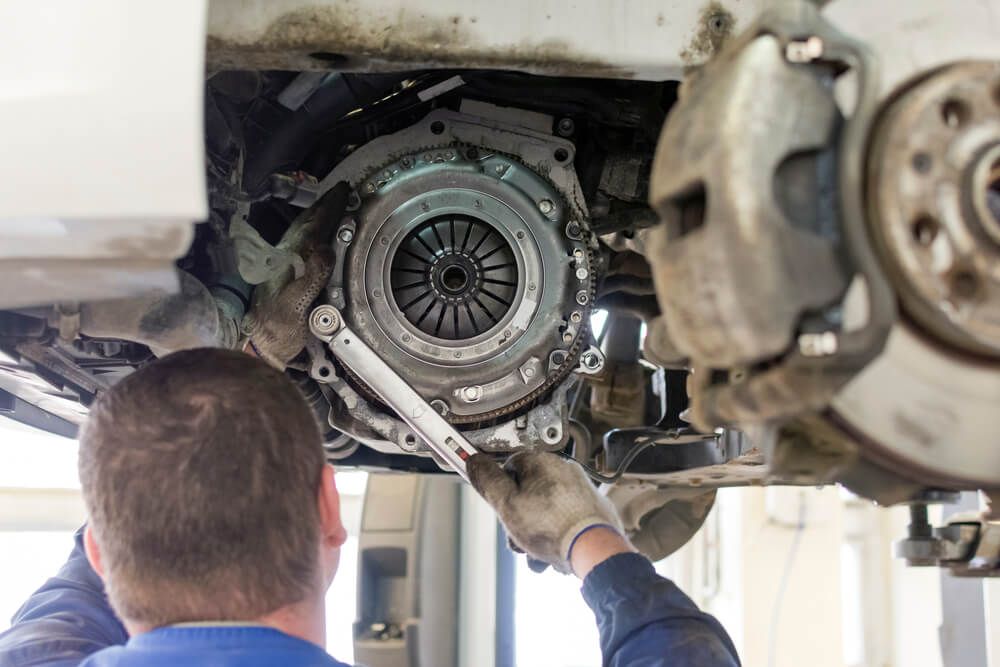 Mechanic working on car clutch assembly using a wrench in a garage.