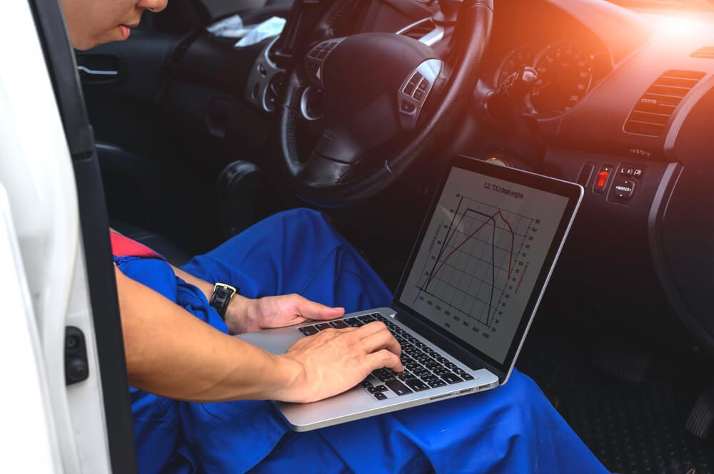 Mechanic using a laptop inside a car, reviewing a graph, presumably for diagnostics.