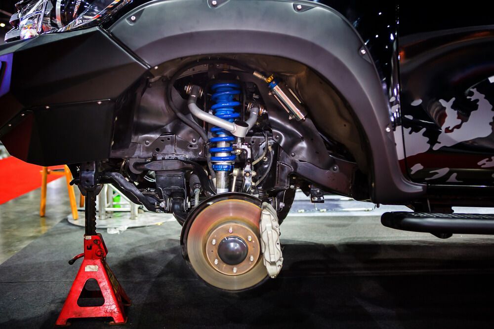 A truck's front suspension on a jack stand. Blue shock absorber, exposed brake rotor, black fender flares.