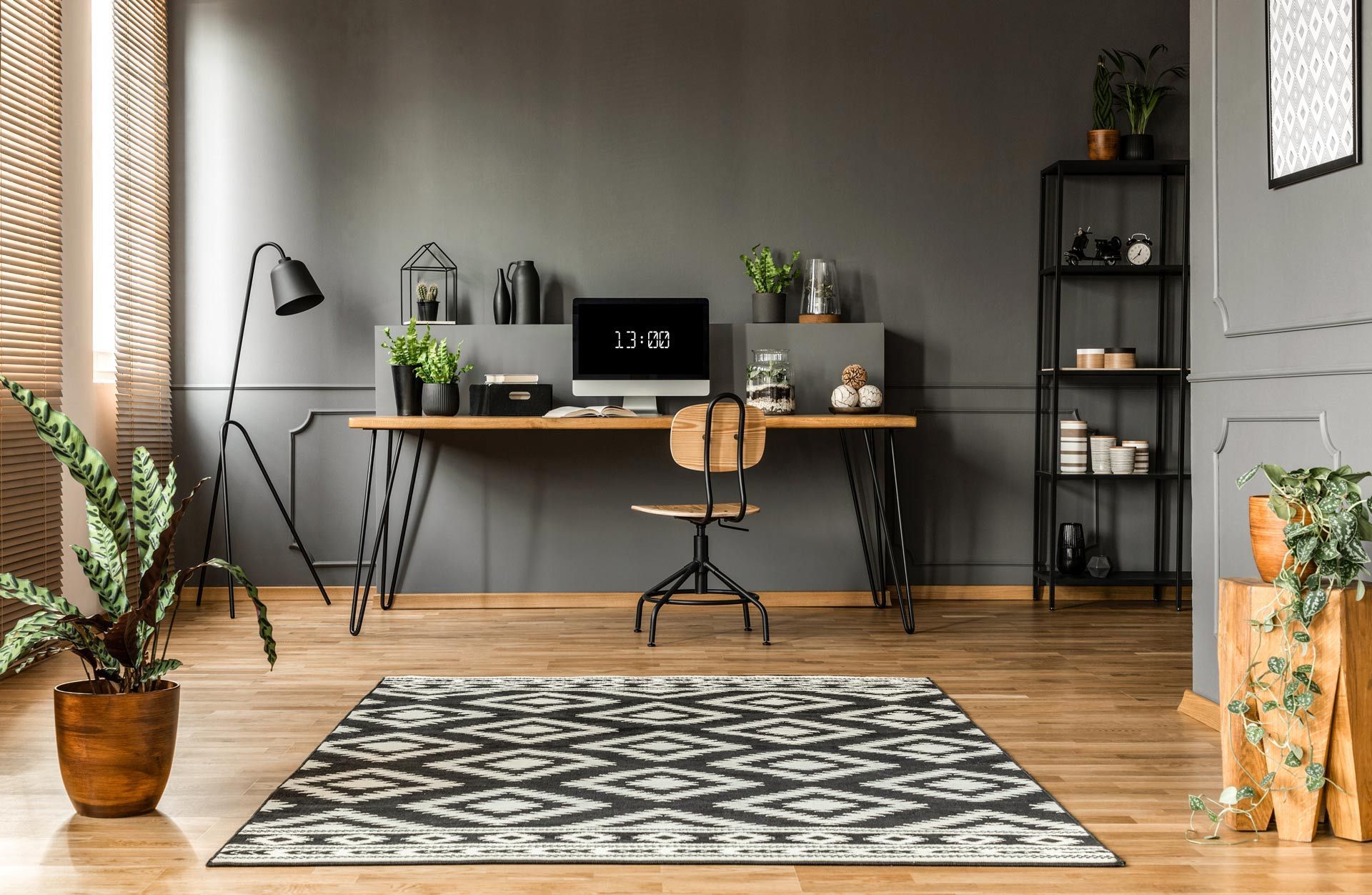 Modern home office with desk, laptop, plants, chair, and patterned rug on wood floor