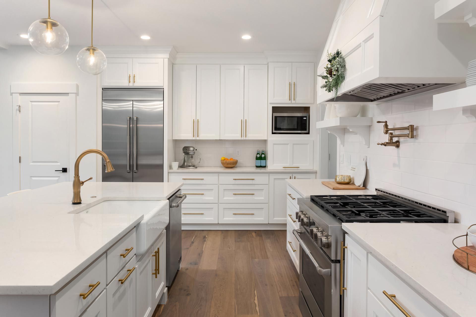 Bright white modern kitchen with island, stainless appliances, gold faucet, and wood floor