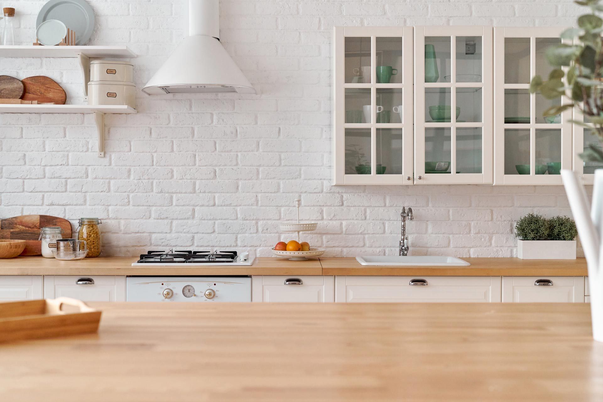 Couple standing in a bright white kitchen, one leaning on the other, with cabinets and hanging penda