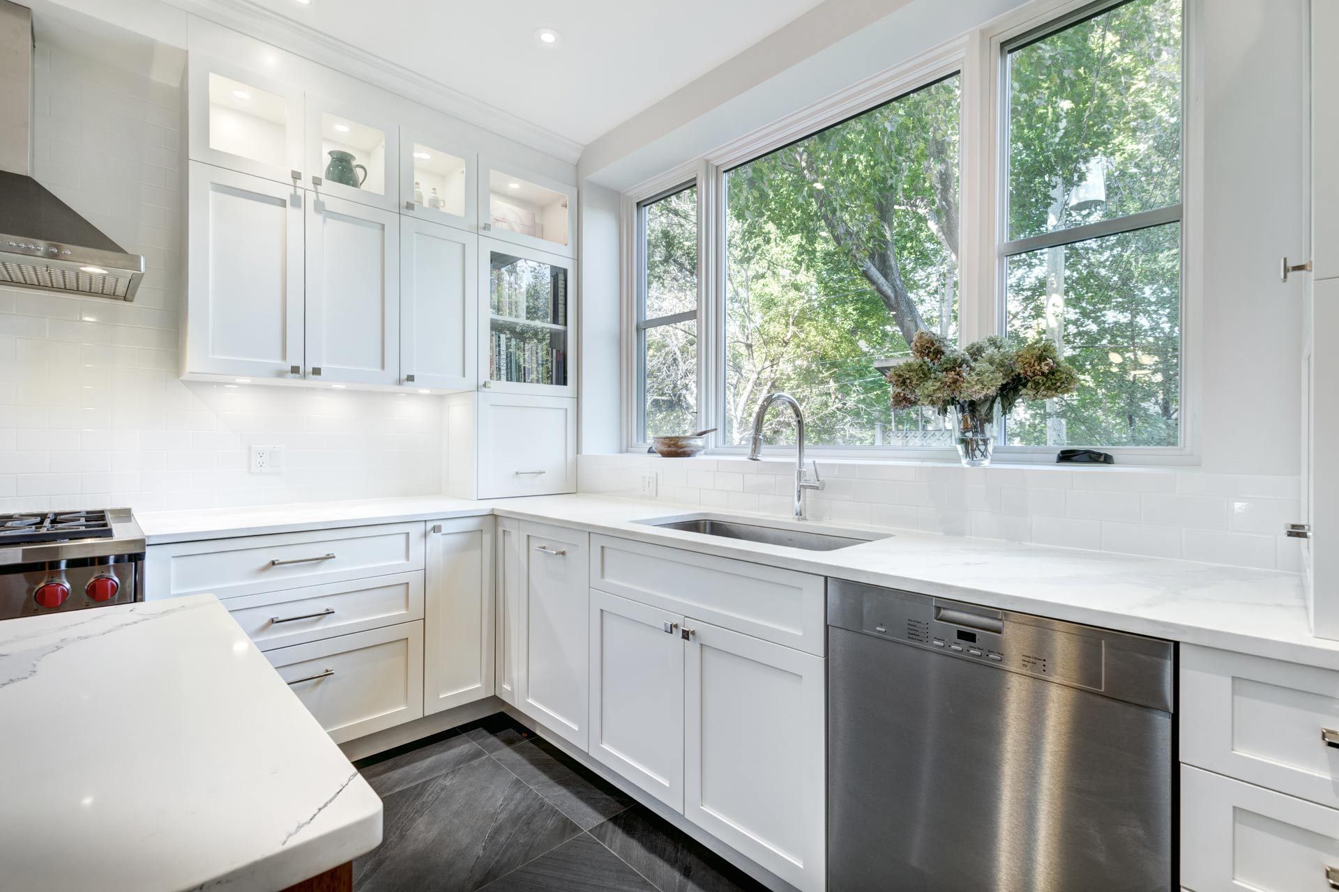 Bright white kitchen with stainless steel dishwasher, large windows, and glossy cabinets