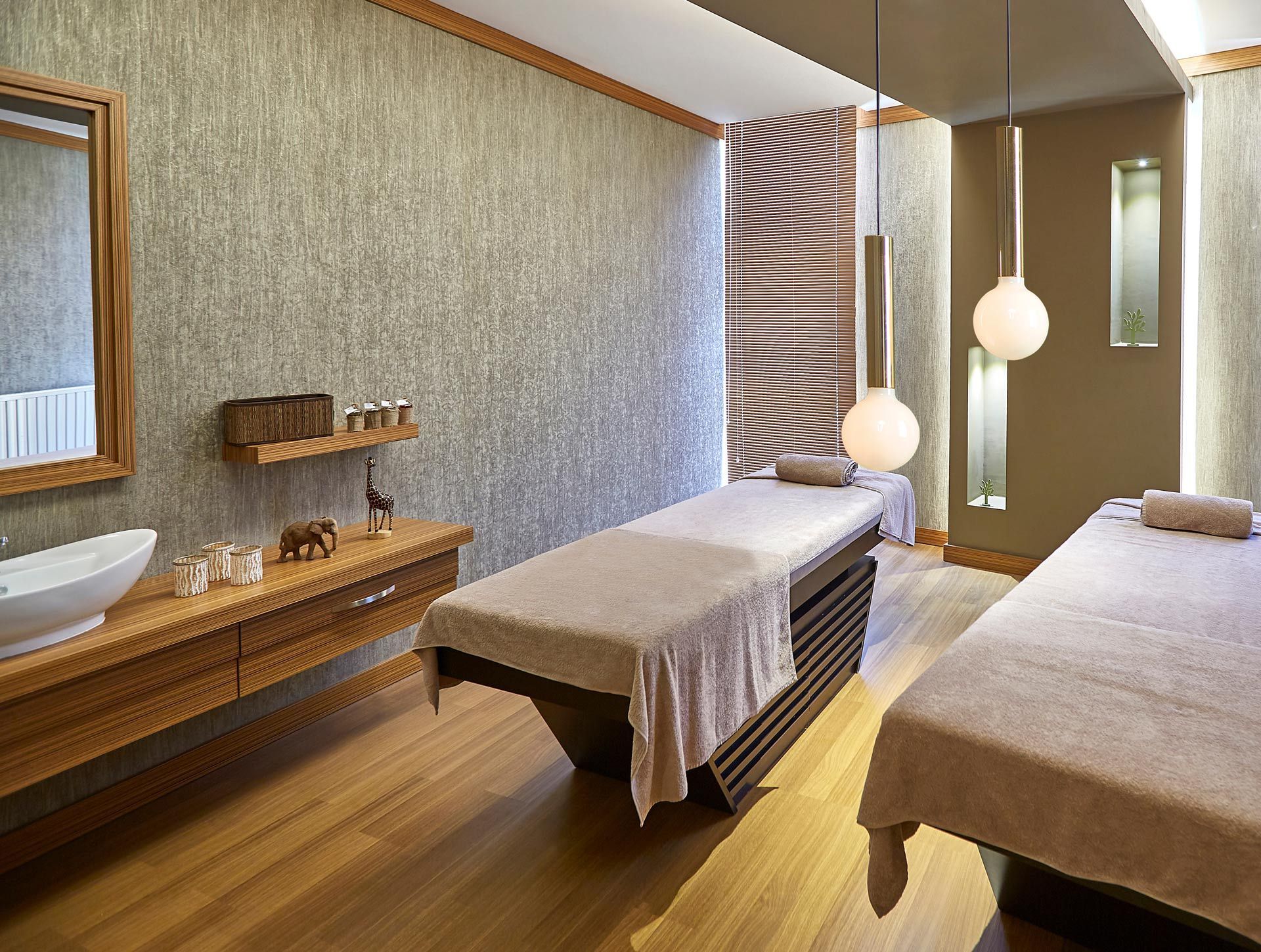 Spa treatment room with two massage tables, wooden sink counter, and warm lighting
