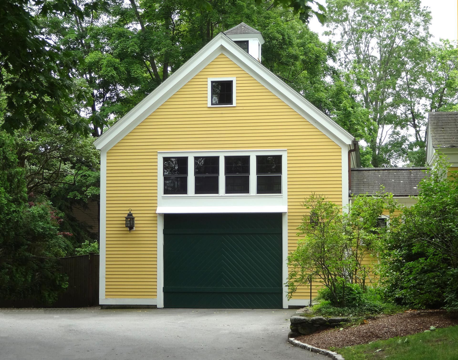 Yellow garage with green door and white trim, surrounded by trees and driveway
