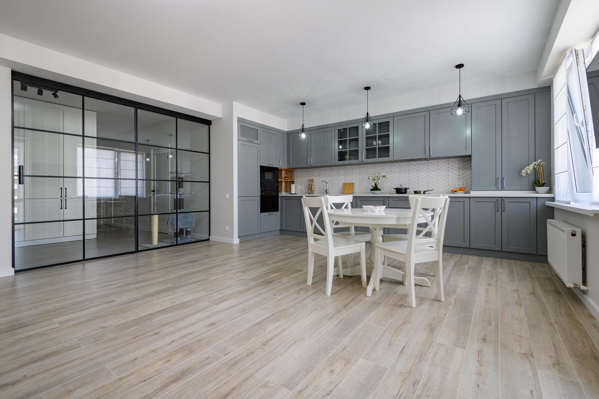 Bright modern kitchen-dining room with gray cabinets, white table, and glass partition doors