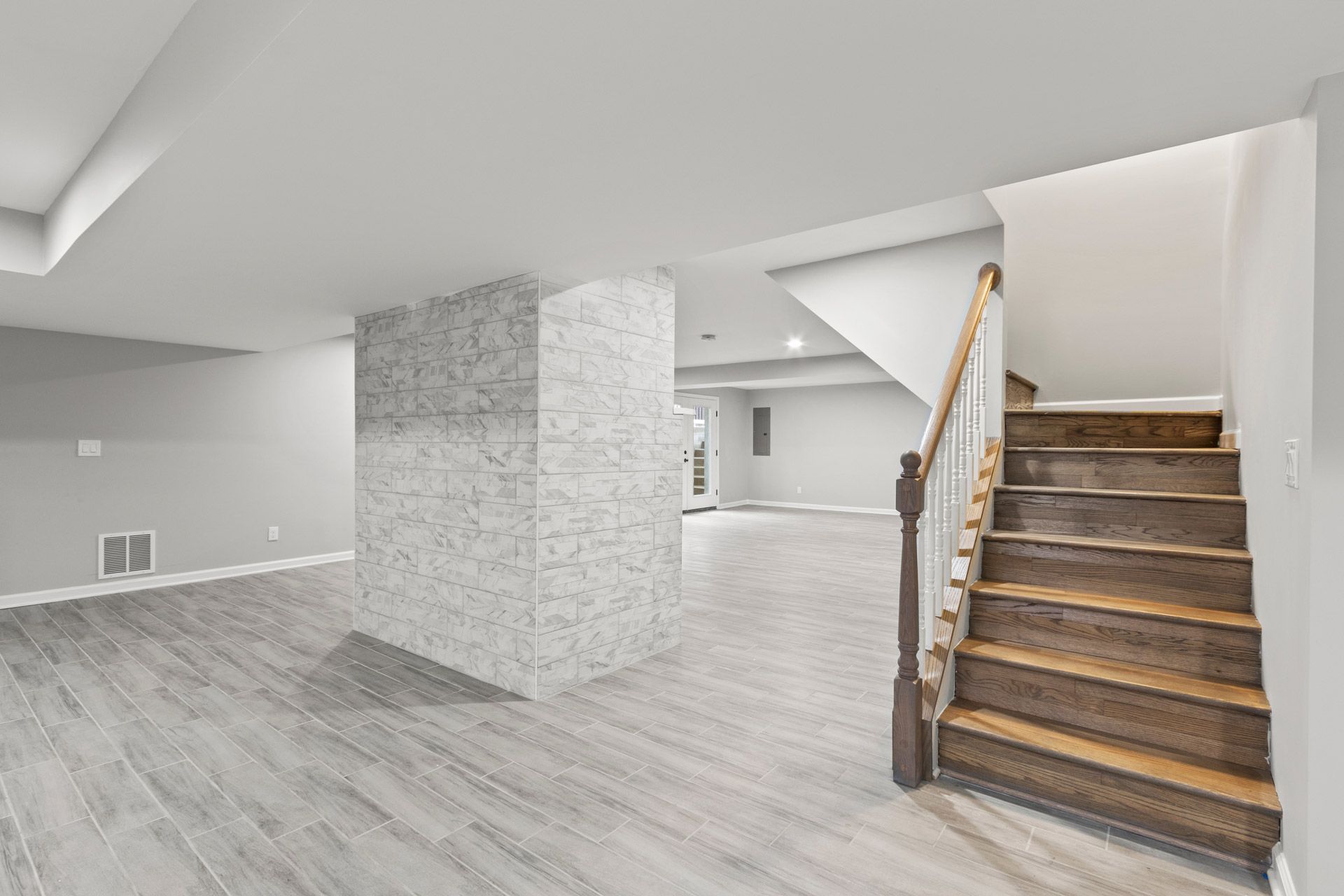 Finished basement with gray flooring, white walls, and carpeted stairs with wooden railing