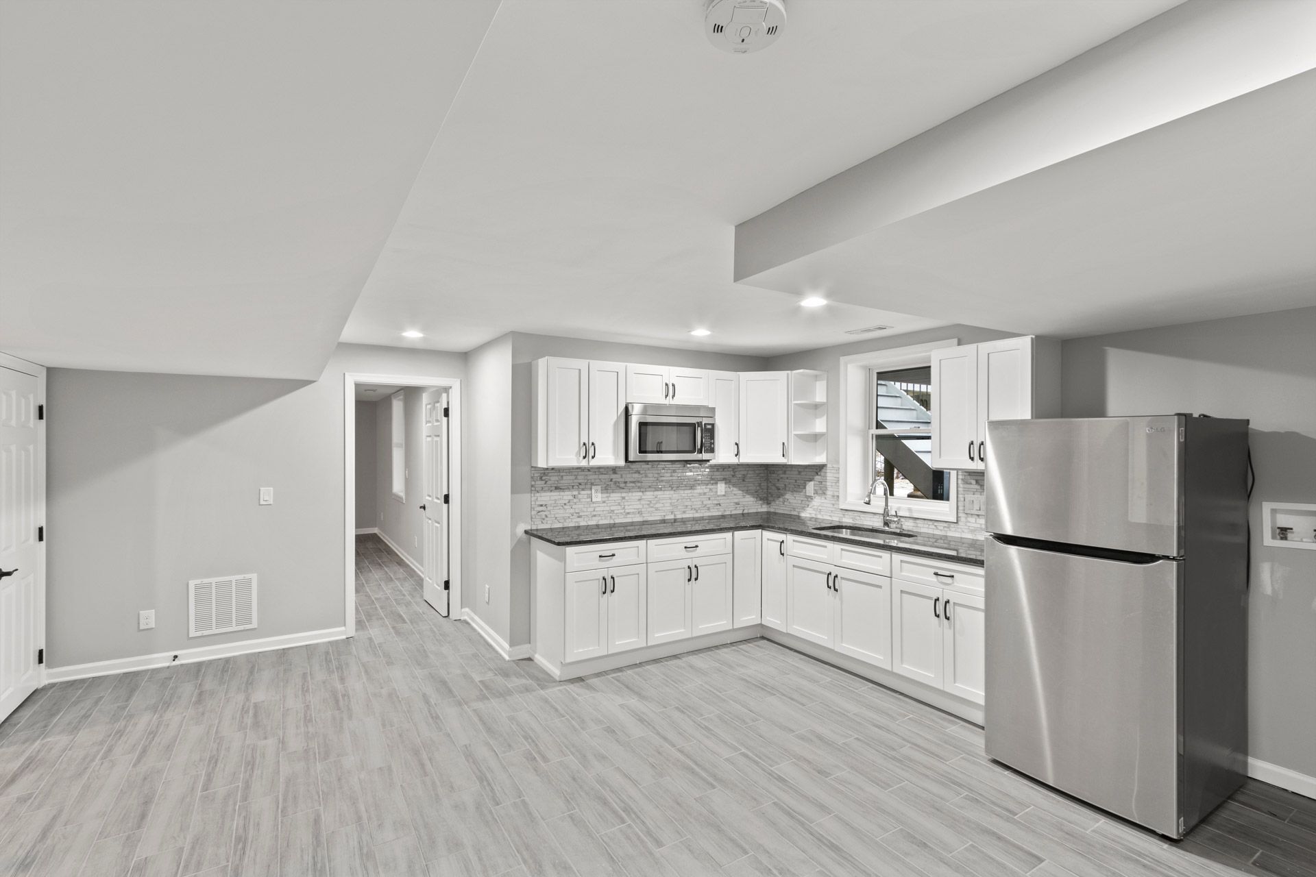 Empty modern kitchen and living area with stainless steel appliances, white cabinets, and gray flooring
