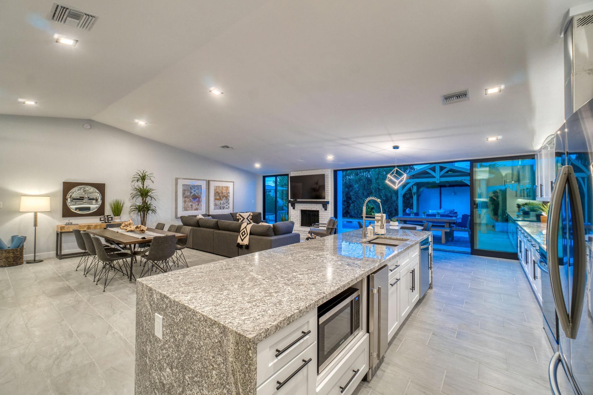 Modern open-plan kitchen and living room with granite island, dining table, gray sofa, and large glass doors to patio