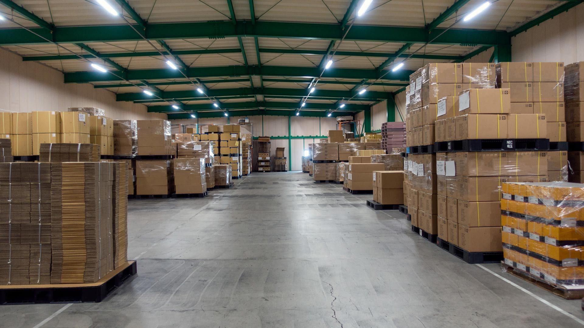 Warehouse aisle with stacked cardboard boxes on pallets under green steel beams