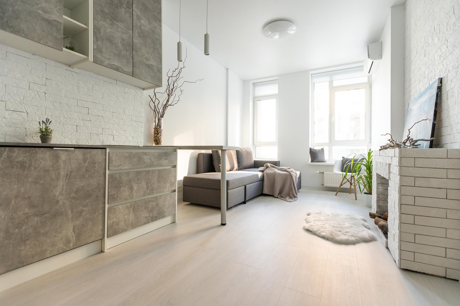 Bright minimalist living room with gray sofa, white walls, large windows, and light wood flooring
